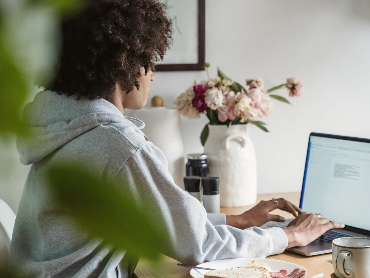 Profissional autônoma trabalhando no notebook em casa, à mesa perto da janela