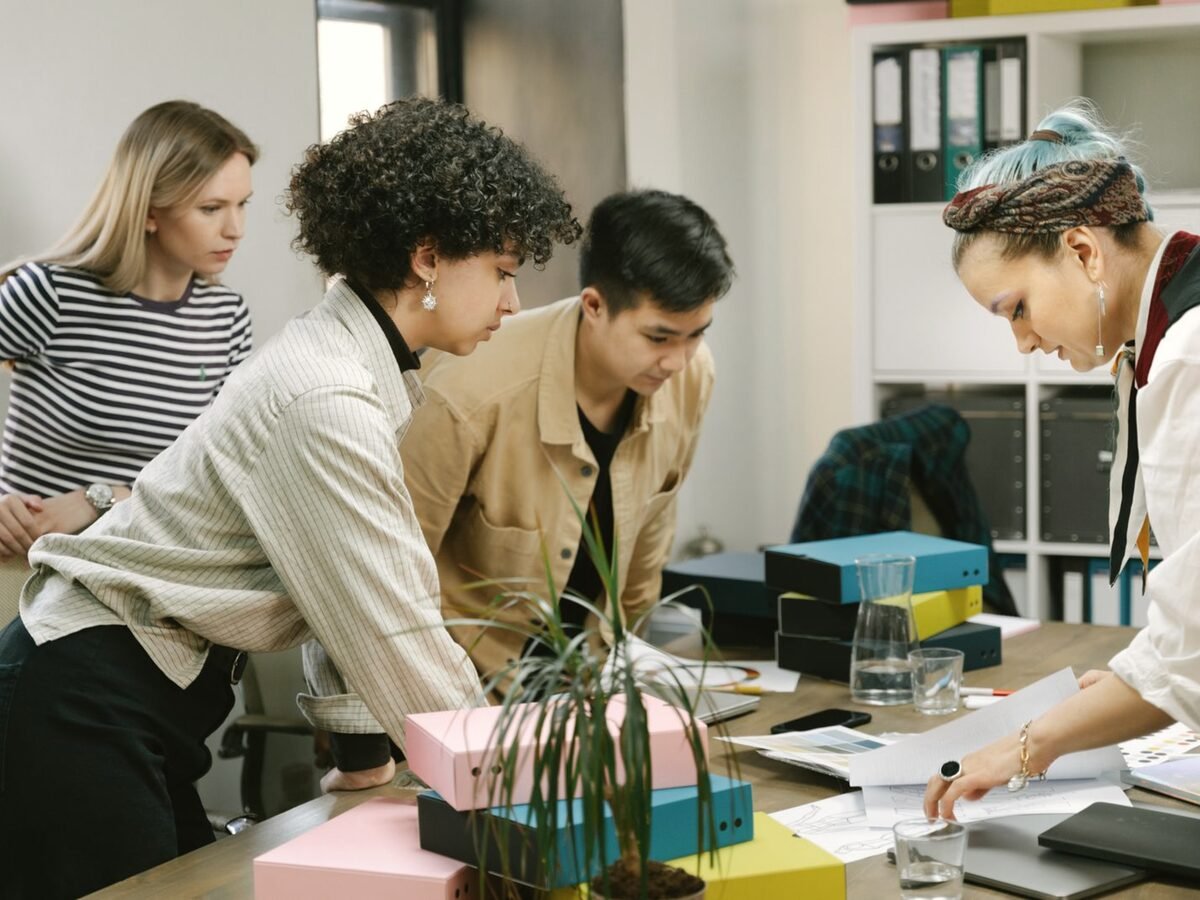 Equipe pequena reunida em volta de uma mesa de escritório, analisando materiais de trabalho